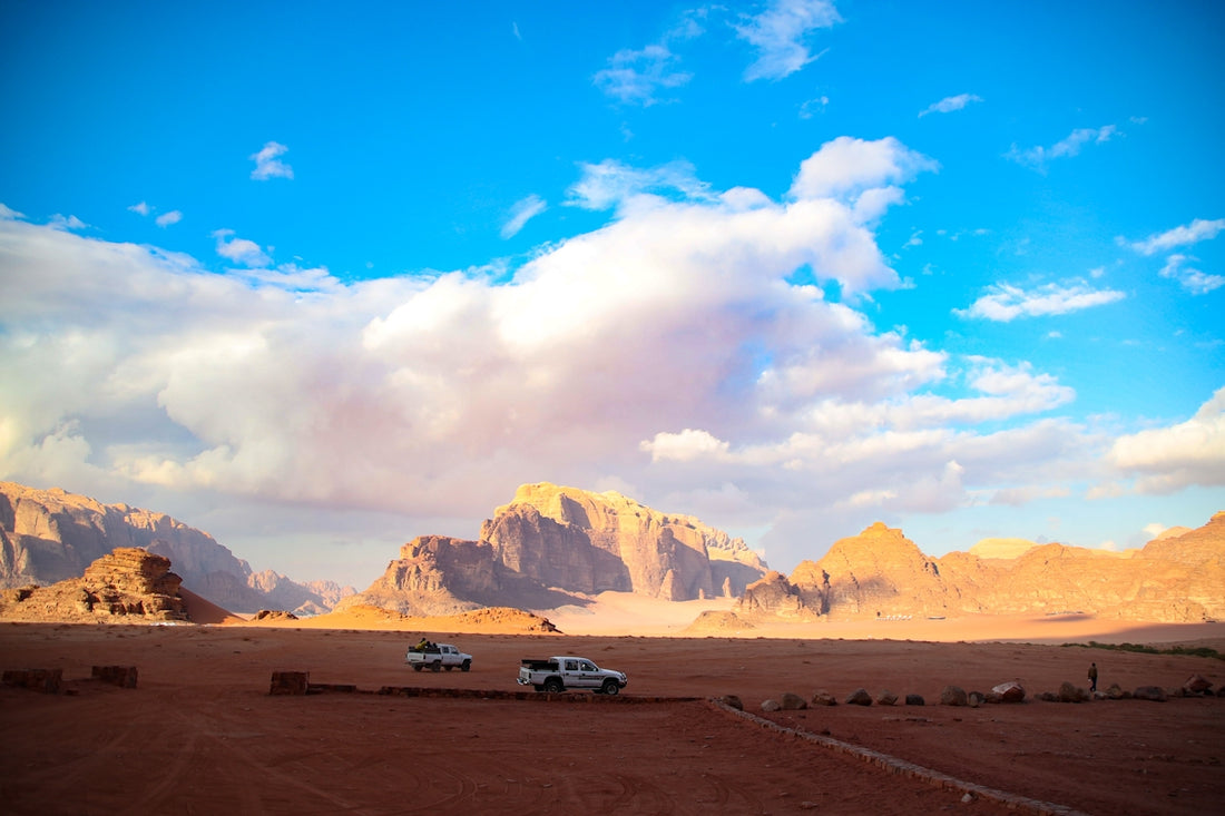 Two cars driving through a desert landscape with mountains.